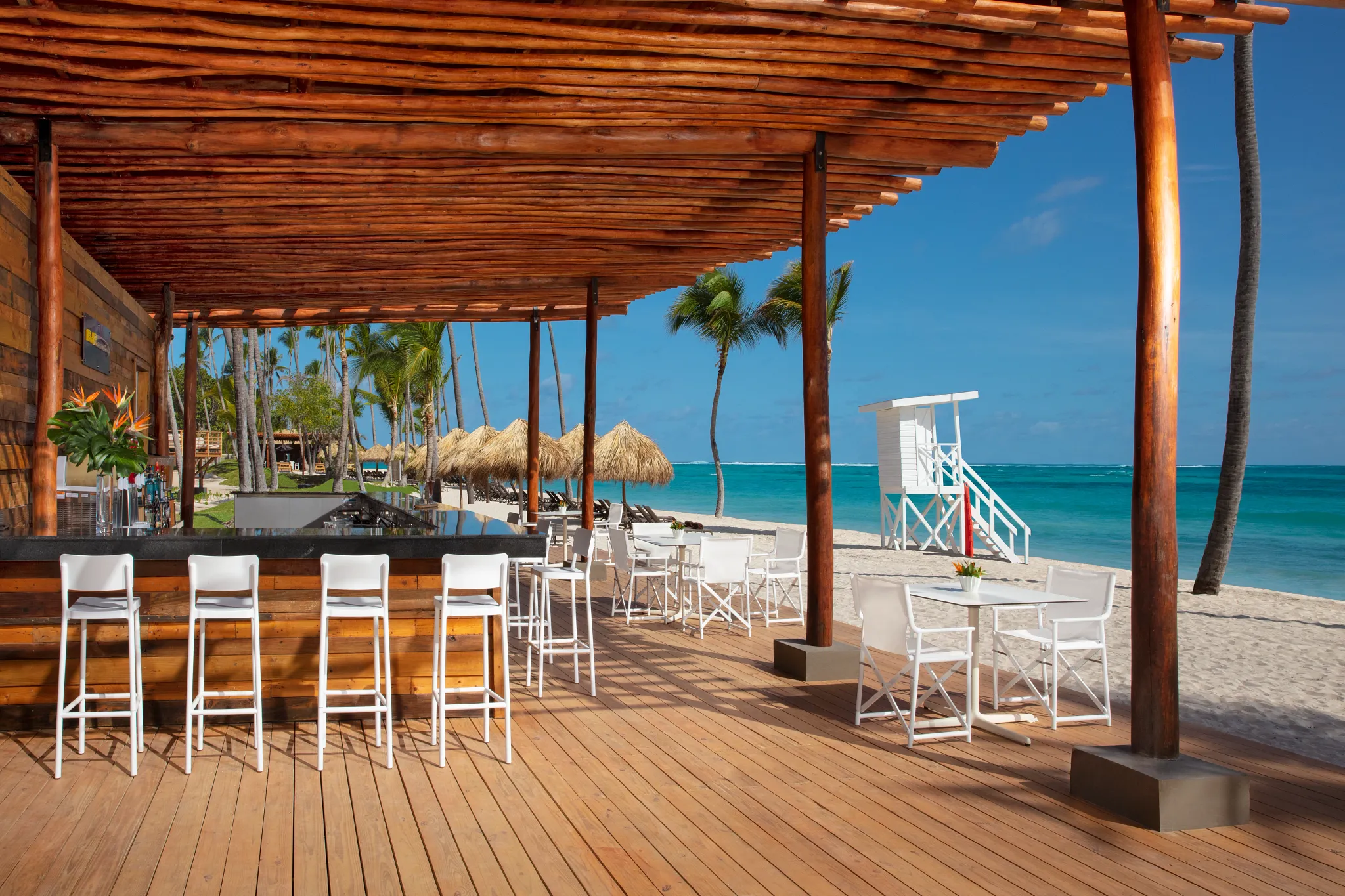 Barracuda beachfront bar at Dreams Flora Resort & Spa with wooden deck seating, ocean views, palm trees, and tropical Caribbean setting.