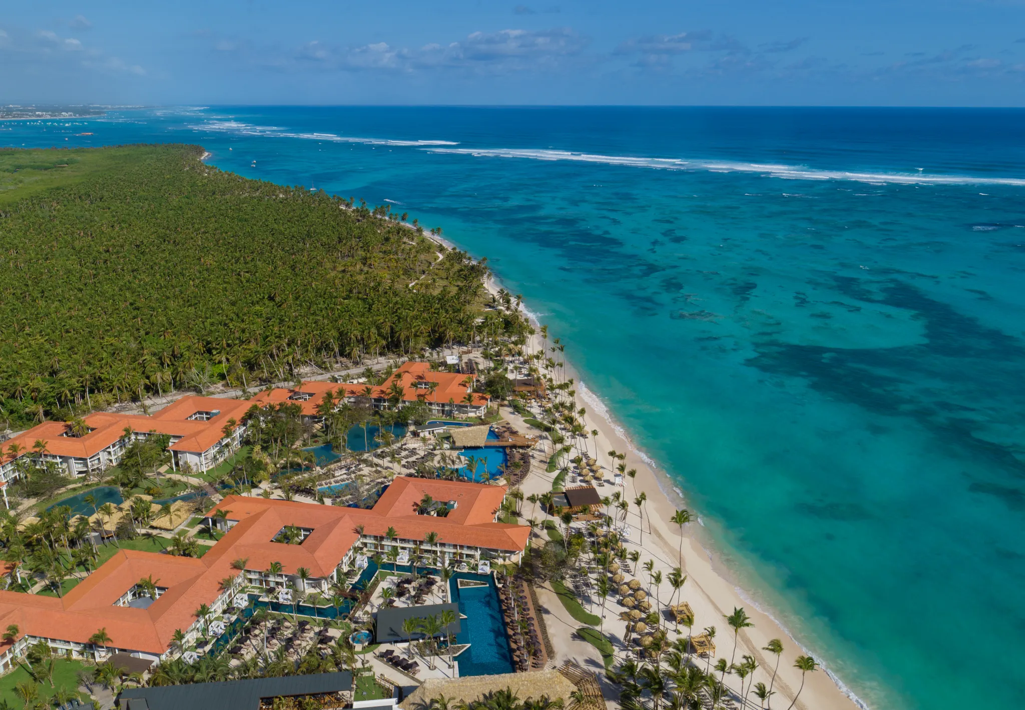 Wide aerial of beachfront pools and white-sand beach at Dreams Flora Resort & Spa in Punta Cana.