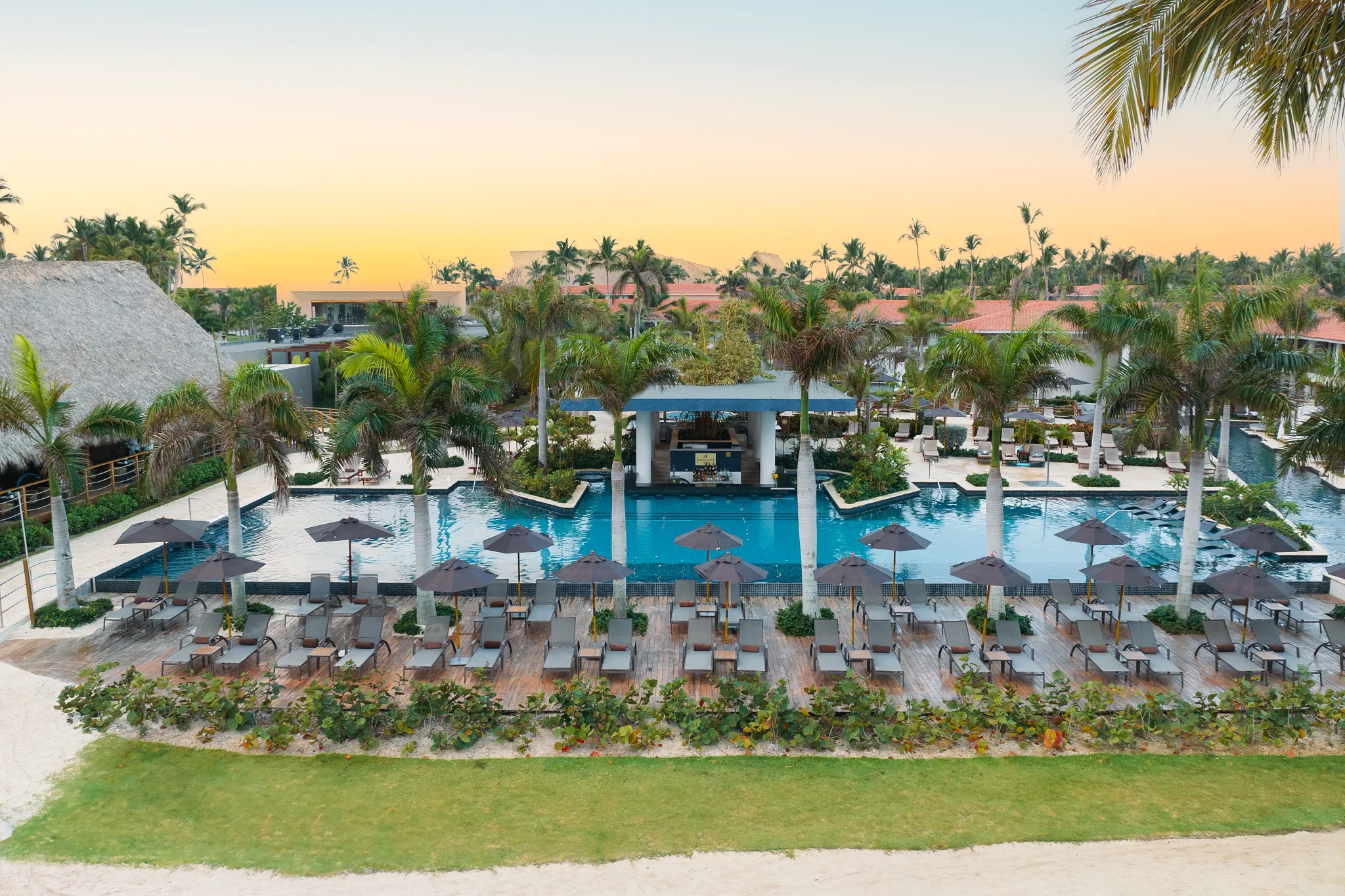 Sunset view of family pool with lounge chairs and pool bar at Dreams Flora Resort & Spa Punta Cana.