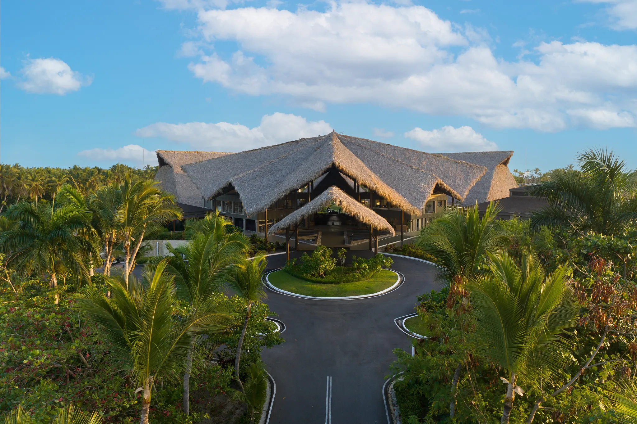 Grand entrance with thatched-roof lobby surrounded by palm trees at Dreams Flora Resort & Spa Punta Cana.
