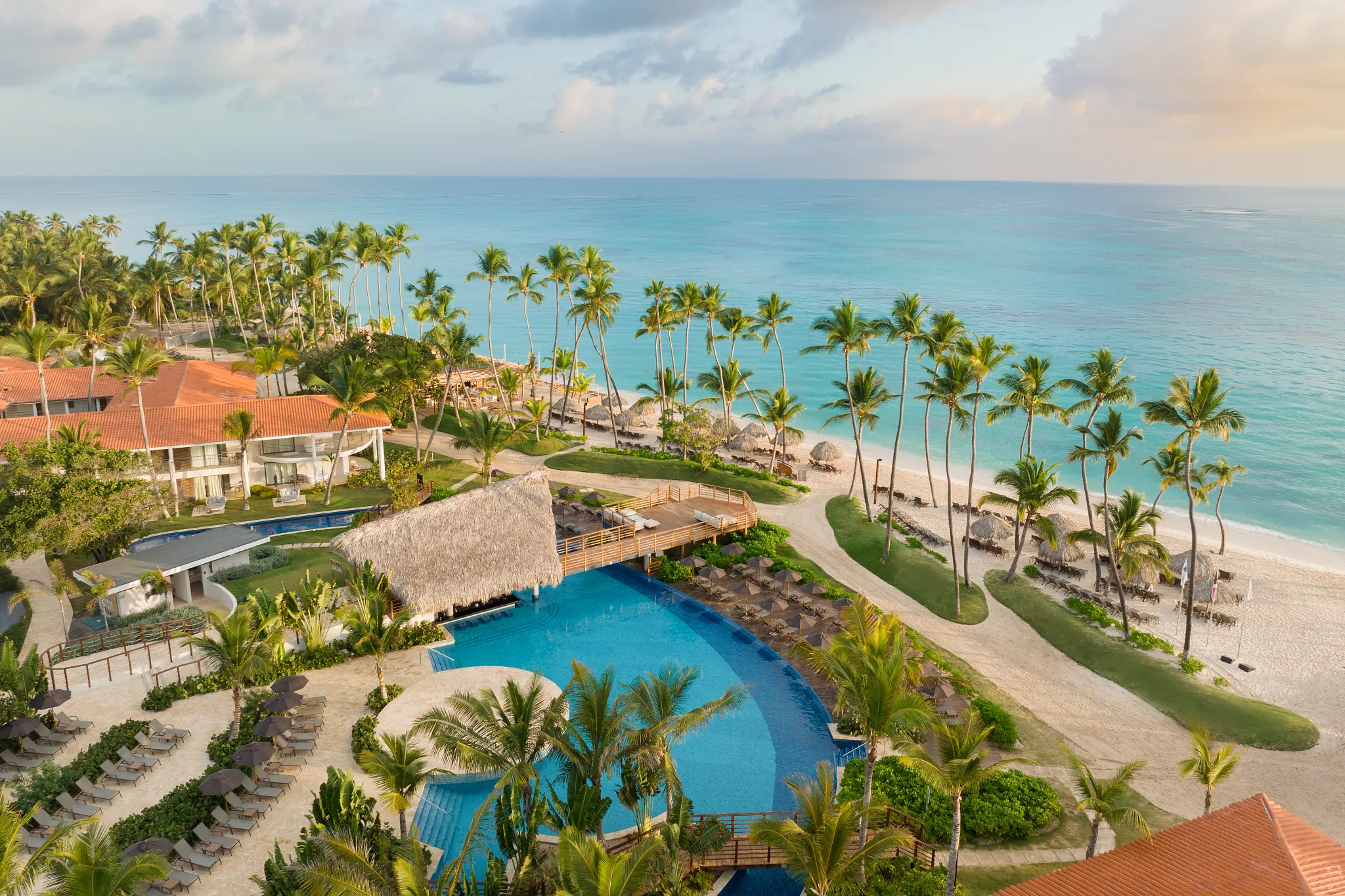 Elevated view of main pool with thatched-roof bar and beach access at Dreams Flora Resort & Spa Punta Cana.